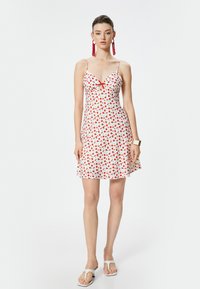 Rood en witte bloemenprint jurk met dunne bandjes, V-hals en een klein strikdetail op de borst; uitlopende rok, lichtgewicht stof.