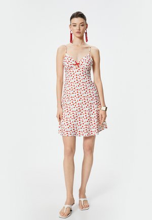 Robe à imprimé floral rouge et blanc avec des bretelles fines, décolleté en V et un petit nœud au niveau de la poitrine ; jupe évasée, tissu léger.