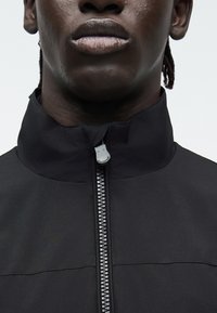 Κοντινή λήψη ενός ατόμου που φοράει μαύρο μπουφάν με φερμουάρ κλειστό μέχρι τον γιακά.