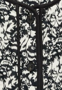 Czarnobiały pikowany materiał w kwiatowy wzór, z okrągłym czarnym guzikiem i czarną lamówką wzdłuż krawędzi.