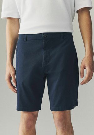 Shorts din bumbac de culoare albastru închis, cu fața dreaptă, închidere cu un singur nasture, buzunare laterale și tăietură până la genunchi. Textură netedă, design casual.