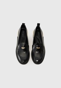 Zwarte gepatenteerde leren loafers met een gouden accent op de band, ronde neus en gestructureerde zijkanten. Flexibele zolen met een laag hakontwerp.