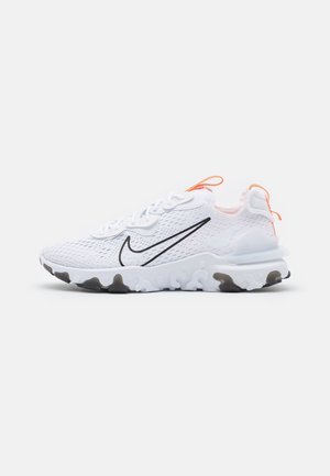 Biały but sportowy Nike z czarnym znakiem, oddychającą siateczkową cholewką, teksturowaną białą podeszwą i pomarańczowymi pętlami na języku i pięcie.