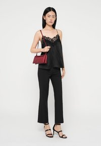 Black satin camisole with lace trim, paired with black flared pants. Model holds a small red handbag and wears black strappy heels.
