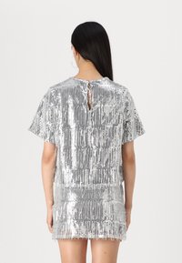 Abito argento con paillettes, maniche corte, vestibilità ampia, dettaglio a chiave sul retro e un design a frange lungo l'orlo.