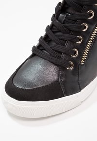 Black high-top sneaker featuring a combination of smooth leather and suede. Includes black laces and gold zipper detail on the side. White sole.