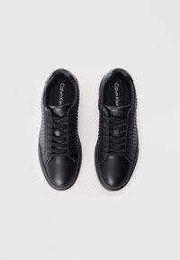 Black leather sneakers with textured sides, round toe, and flat laces. Features Calvin Klein branding on the tongue and insole.