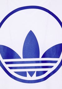 Weißes T-Shirt mit einem großen blauen Adidas Trefoil-Logo, das aus drei Blättern und horizontalen Streifen darunter besteht. Glatte Textur.