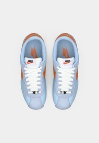 Nike tenisice s svijetloplavom gornjom djelom, narančastim bočnim swoosh-om i bijelim vezicama. Imaju podstavljena vrata i teksturiranu tkaninu za bolje prianjanje.