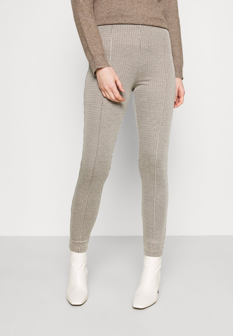 Hochtaillierte Leggings im Hahnentritt-Muster, aus Strickstoff gefertigt, mit einer enganliegenden Passform und kombiniert mit weißen Knöchelstiefeln.