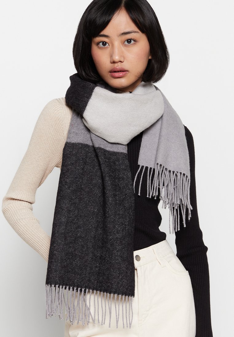 Gestrickter Schal mit grauen und schwarzen Farbblocken, verziert mit feinen Fransen. Hergestellt aus weichem Material, fällt er elegant um den Hals.