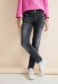 Jeans de mezclilla negra con corte ajustado, textura desgastada y puños remangados, combinados con zapatillas blancas y un suéter de punto rosa.