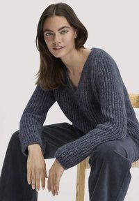 Dunkelblauer gerippter Strickpullover mit V-Ausschnitt und weiten Ärmeln, kombiniert mit passenden Cordhosen, präsentiert vor einem neutralen Hintergrund.