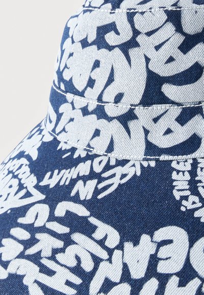 Κοντινό πλάνο ενός καπέλου τύπου bucket από τζιν με λευκά γράμματα σε στυλ γκράφιτι και αφηρημένα σχήματα εκτυπωμένα σε όλο το σκουρομπλε φόντο.