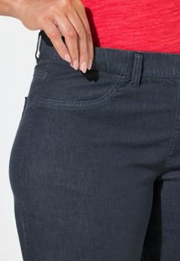 Jeans de denim oscuro con un diseño ajustado, costuras sutiles y bolsillos delanteros. La mano descansa sobre la cintura para dar un enfoque visual.