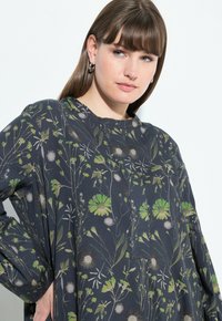 Dunkelblumiges Tunika mit Rundhalsausschnitt und langen Ärmeln. Mit grünen und weißen Blumen auf einem marineblauen Hintergrund.