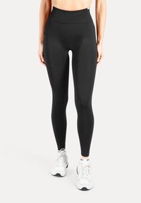 Schwarze Leggings mit hoher Taille aus elastischem Stoff, mit einer Seitentasche und glatter Textur, kombiniert mit weißen Sportschuhen.