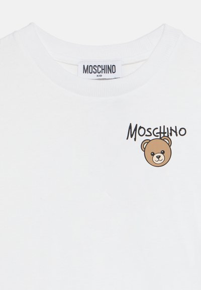 Λευκό παιδικό T-shirt με ετικέτα της μάρκας Moschino και μικρό γραφικό αρκουδάκι δίπλα στο κείμενο Moschino στο στήθος.