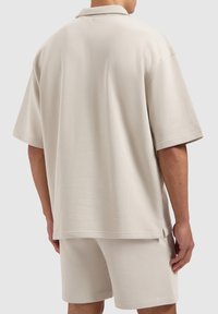 Beige polo shirt met korte mouwen, gemaakt van zachte stof, met een kraag en een losse pasvorm, gecombineerd met bijpassende shorts.