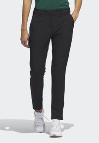 Svarta, figurnära träningsbyxor tillverkade av elastiskt material, med sidofickor och en slät yta, kombinerade med vita träningsskor.