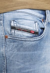 Vaaleansiniset farkut, joissa on näkyvä takatasku. Musta ja punainen etiketti "Diesel Industry" näkyy taskun yläpuolella. Farkeissa on kevyt kuluminen.