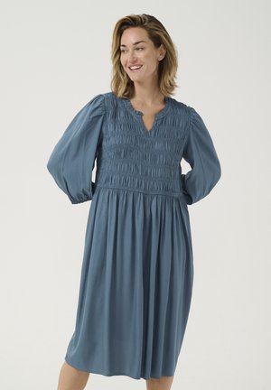 Robe bleu clair, longueur genoux, avec un corsage froncé et des manches longues bouffantes. Dotée d'une encolure arrondie et d'une jupe fluide. Texture lisse.