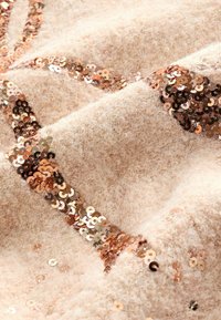 Lichtbeige textiel met een pluche textuur, aangevuld met een strook glanzende roségouden pailletten. Details met verspreide pailletten zijn aanwezig.