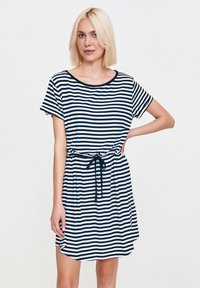 Kobieta z blond bobem uśmiecha się, nosząc casualową sukienkę w granatowo-białe paski, zaznaczoną w talii sznurkiem.