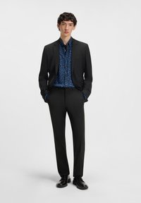 Black suit with a single button and notched lapel, paired with a blue patterned shirt. Leather shoes complete the look.