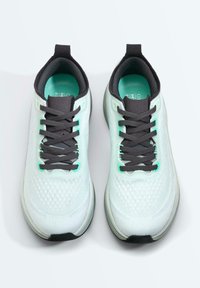 Paire de chaussures de course blanches avec des lacets noirs et des semelles intérieures turquoise, vues de dessus sur un fond blanc uni.