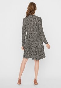 Svart klänning med vita prickar, långa ärmar och figurnära midja. Har en flerlagerskjol och mjuk tygtextur.