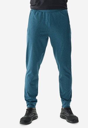 Pantalones deportivos ligeros y azules con bolsillos laterales y un ajuste tapered, fabricados con un material transpirable. Combinados con zapatillas negras.