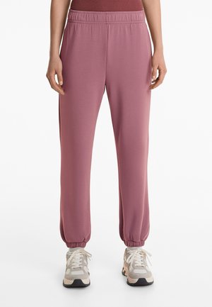 Pantaloni jogger de culoare roz deschis, cu talie elastică și manșete, confecționați dintr-un material neted și elastic. Prezintă o croială lejeră și buzunare laterale.