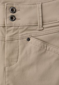 Los pantalones de tela beige presentan una textura suave con dos botones metálicos en la cintura, costuras detalladas y una abertura de bolsillo diagonal.