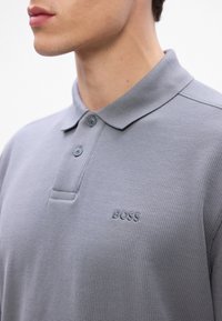 Szara koszulka polo wykonana z teksturowanej tkaniny, z klasycznym kołnierzykiem, dwoma guzikami oraz wyszywanym logo "BOSS" na lewej piersi.