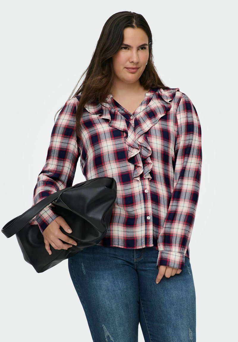 Camicia a quadri rossa, blu navy e crema con rouches lungo il colletto. Abbinata a una borsa a tracolla nera e jeans blu.