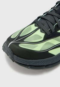 Črni in svetlo zeleni tekaški čevelj z teksturirano zgornjo plastjo, mrežastimi detajli in elegantnimi vzorci. Ima vezalke in gumijast podplat za dober oprijem.