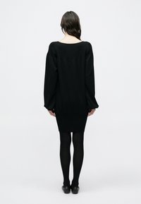 Μαύρο πλεκτό φόρεμα με μακριά φουσκωτά μανίκια, εφαρμοστή μέση και ριμπ τελείωμα. Φορεμένο με μαύρο καλσόν και παπούτσια τύπου slip-on. Λείο υλικό, μινιμαλιστικός σχεδιασμός.