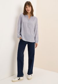 Blusa leggera a righe con maniche lunghe e colletto con bottoni. Indossata con jeans a gamba larga blu scuro e sneaker bianche con dettagli neri.