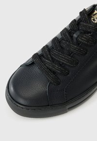 Baskets en cuir noir avec finition texturée, bout rond, lacets noirs et semelle en caoutchouc. Présente des détails de couture subtils le long des côtés.