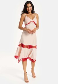 Peach-colored dress with red lace accents across the waist and hem. Spaghetti straps and a flowing asymmetrical skirt design. Smooth texture.