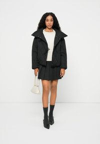 Μαύρο πουπουλένιο μπουφάν με μεγάλα γιακά, λευκό πουλόβερ, γκρι φούστα με πτυχώσεις, γκρι γόνατο ψηλές κάλτσες και μαύρα μυτερά τακούνια. Μικρή λευκή τσάντα.