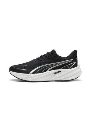 Zapatilla de correr Puma en blanco y negro con suela gruesa acolchada y diseño de raya plateada en el lateral, mostrada desde un perfil derecho.
