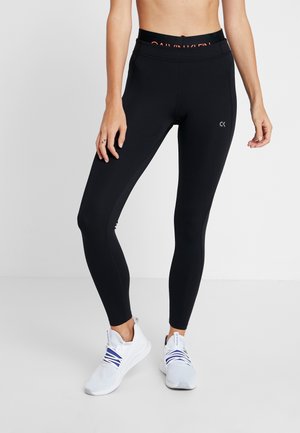 Leggings noirs avec une large taille comportant "Calvin Klein" en orange contrasté. Tissu lisse et extensible avec des détails sur les panneaux latéraux.