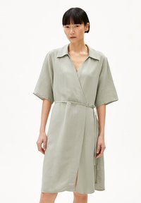Light green wrap dress in a smooth fabric; features a collar, short sleeves, and a tie belt. Notable side slit and minimalist design.