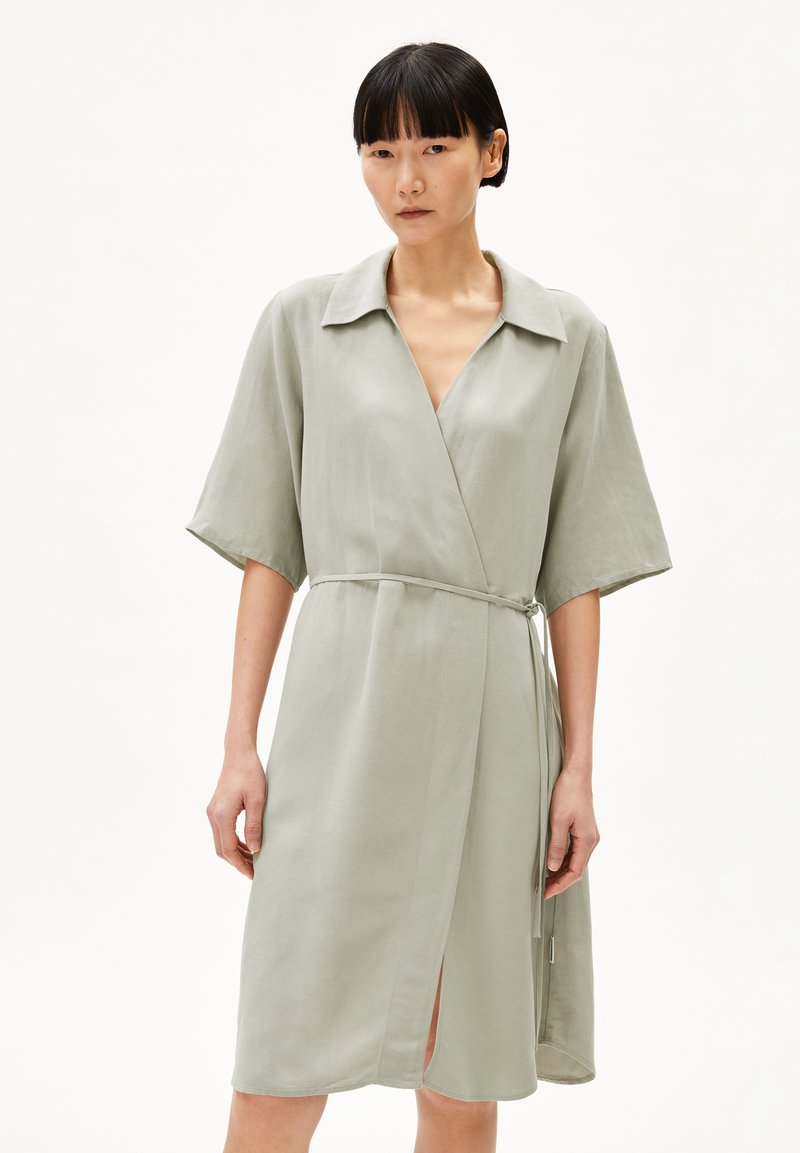 Light green wrap dress in a smooth fabric; features a collar, short sleeves, and a tie belt. Notable side slit and minimalist design.