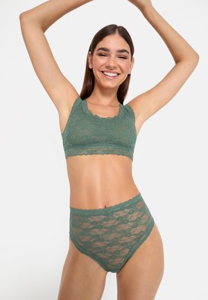 Kant bralette en hooghangende slipjes in gedempt groen. Kenmerkend zijn de golvende randen en het bloemenpatroon. Lichtgewicht, semi-doorschijnende textuur.