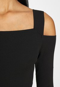 Schwarzes, geripptes Oberteil mit quadratischem Ausschnitt und kalten Schultern sowie enganliegenden langen Ärmeln. Glatte Textur und minimalistischem Stil.