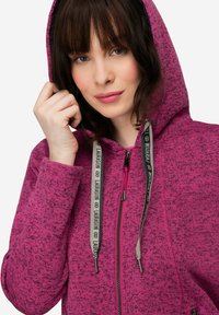 Fleece hoodie i stark rosa med texturerat tyg, dragkedjeslutning och dragsko med logotypdetaljer. Huva och sidofickor.