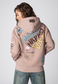 Pullover hoodie in zachte beige stof met kleurrijke grafische prints, waaronder bloemen en tekst. Bevat een capuchon met trekkoord en ribgebreide manchetten.